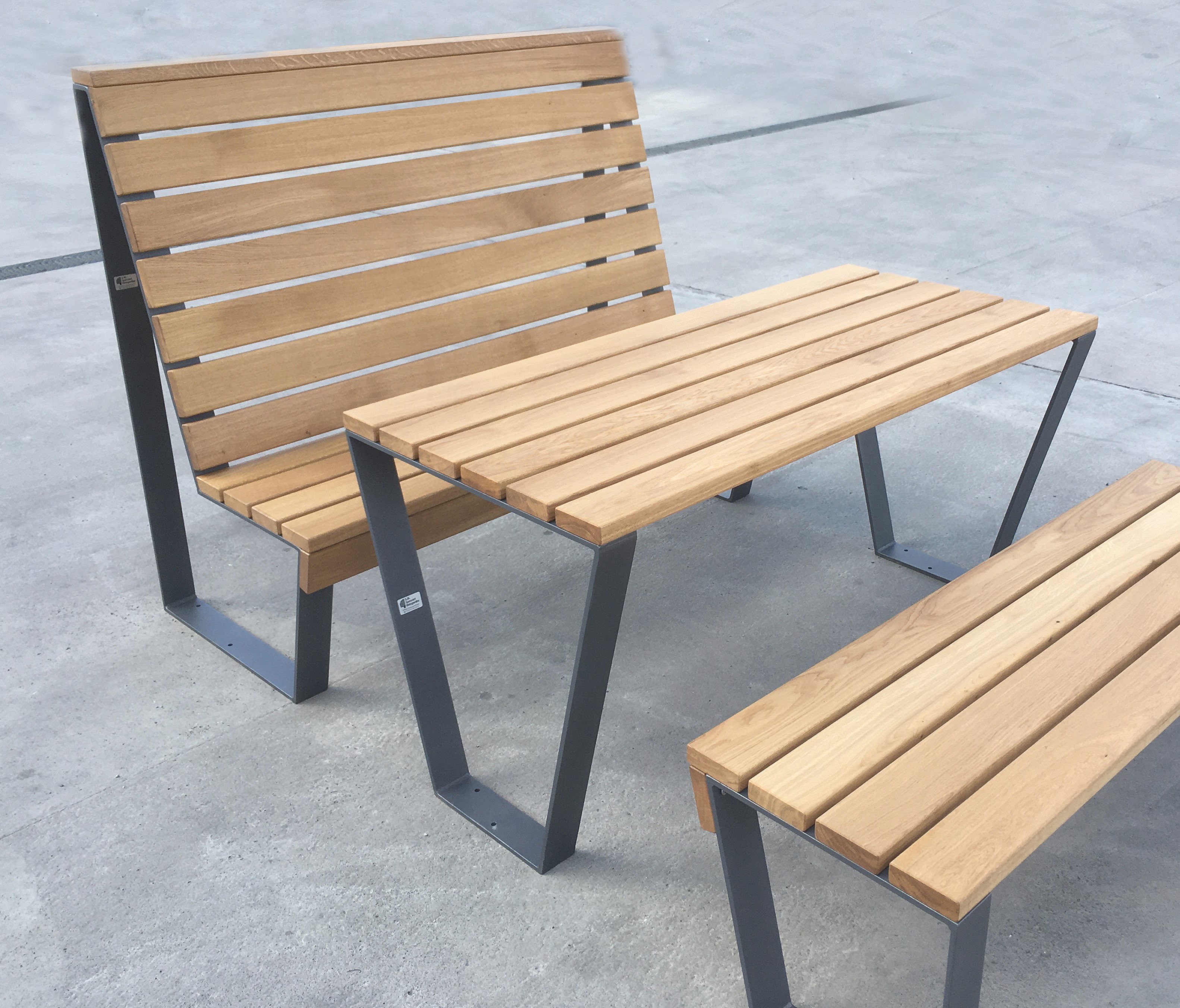 Sitzgruppe aus Bank ohne Lehne, Tisch, Bank mit Lehne, jeweils mit Stahluntergestell und Auflagehölzern aus Eiche. Sitzgruppe Typ "Holz-klasse!"